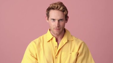 Makyajlı kızgın adam pembe bir stüdyoda kollarını kavuşturarak hareket etmiyor.