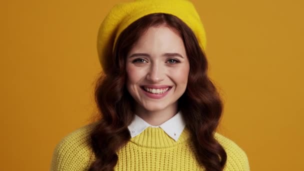 在一个黄色的工作室里 一个戴着贝雷帽的微笑妇女的画像用食指触摸着她的脸颊 — 图库视频影像