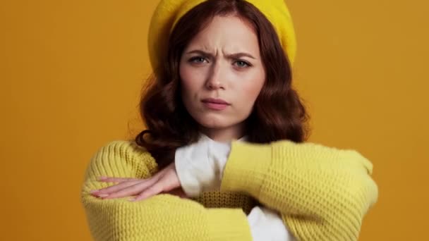 在一个黄色的工作室里 一个戴着贝雷帽的被冒犯的女人交叉着双臂向一边望去 — 图库视频影像