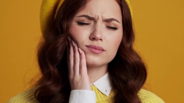 黄色のスタジオで歯痛に苦しんでいる悲しい女性のクローズアップショット — ストック動画