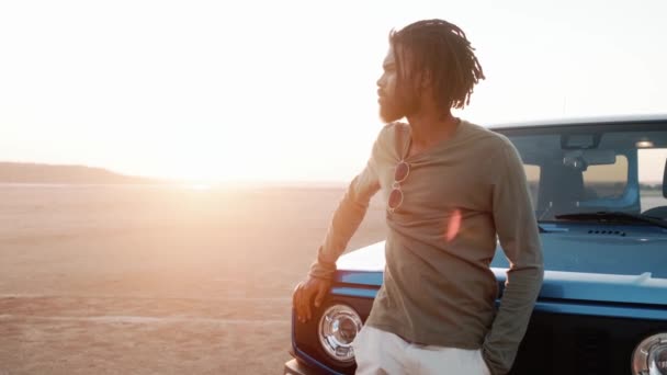 Αφρικανός Στέκεται Δίπλα Στο Αυτοκίνητο Μπροστά Από Ηλιοβασίλεμα Στην Άμμο — Αρχείο Βίντεο