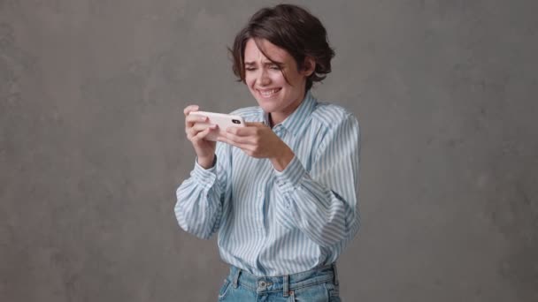 Mujer Entusiasta Jugando Por Teléfono Sonriendo Mientras Está Pie Estudio — Vídeo de stock