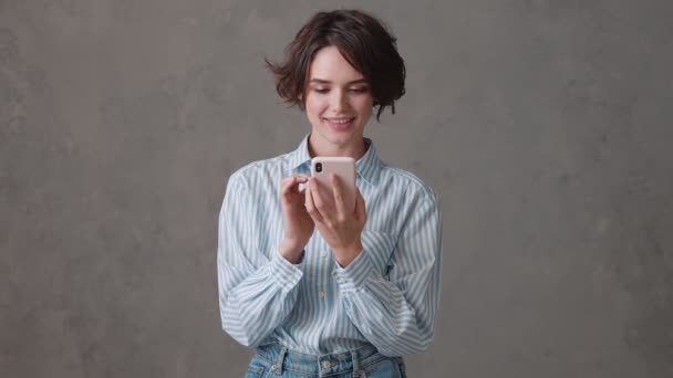 Eine Überraschte Frau Blättert Einem Grauen Studio Telefon Und Jubelt — Stockvideo