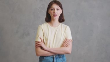 Sarı tişörtlü mutlu kız gri stüdyoda dikilirken olumlu şekilde başını sallıyor.