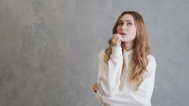 Kapüşonlu, kara kara düşünen bir kadın gri bir stüdyoda dururken kendine iyi bir seçenek sunuyor.