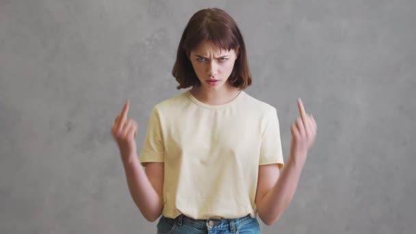 Dziewczyna Pomarszczonym Czołem Pokazuje Środkowy Palec Przed Kamerą Stojąc Szarym — Wideo stockowe