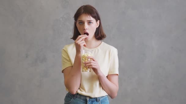 Een Verrast Meisje Dat Popcorn Eet Terwijl Een Grijze Studio — Stockvideo