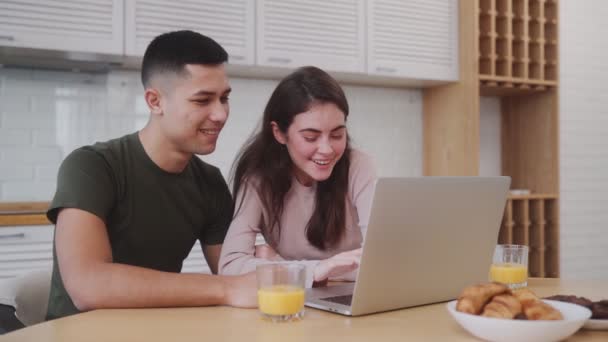 キッチンに座っている間 笑顔のカップルは ノートパソコンで何かを探して 朝食時にカメラを振って — ストック動画