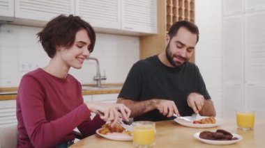 Memnuniyet duyan erkek ve kadın kahvaltı yapıyorlar. Evdeki mutfaktaki masada oturuyorlar.