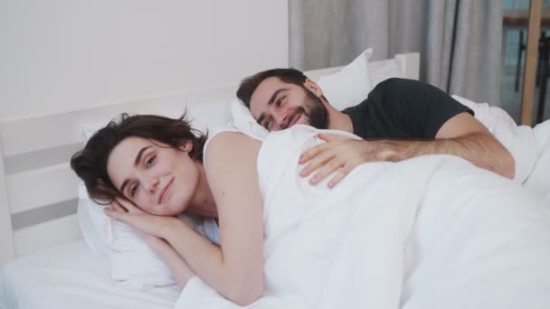 当男人在家里的白色床上叫醒他的女朋友时 一对快乐的年轻夫妇正在睡在一起 — 图库视频影像