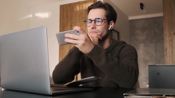 Hombre Sorprendido Con Gafas Sentado Frente Portátil Mirando Teléfono Habitación — Vídeos de Stock