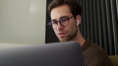 Dizüstü bilgisayara bakıp çizgili odada dudaklarını yalayan konsantre adamın yakın görüntüsü.