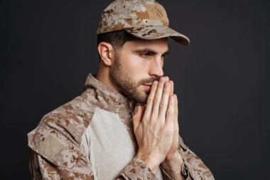 Odaklanmış erkeksi asker siyah arka planda izole edilmiş dua jestleri yapıyor.