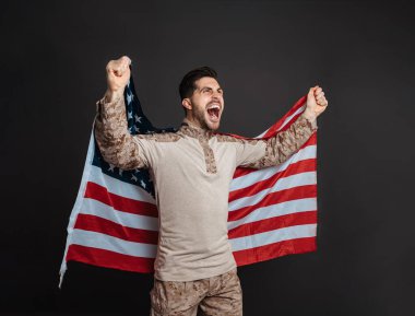 Heyecanlı asker, siyah arka planda izole edilmiş Amerikan bayrağıyla poz verirken çığlık atıyor.