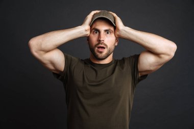 Şok olmuş bir asker şaşkınlığını dile getiriyor ve siyah arka planda kafasını tutuyor.