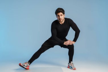 Genç sporcu, mavi arka planda tek başına çalışırken egzersiz yapıyor.