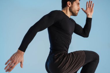 Genç sporcu, mavi arka planda tek başına çalışırken egzersiz yapıyor.