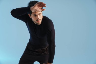 Mavi arka planda tek başına çalışırken yorgun sporcu dinleniyor.