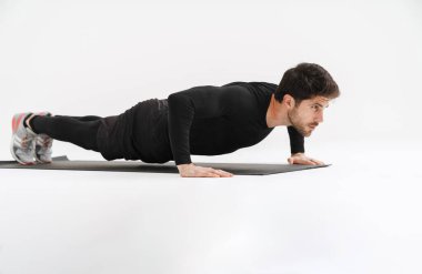 Genç atletik sporcu, beyaz arka planda izole bir şekilde paspas üzerinde çalışırken egzersiz yapıyor.