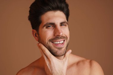 Gülümseyen ve yüzünü ovuşturan mutlu erkek bej arka planda izole edilmiş.