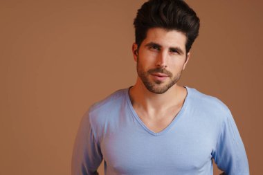 Memnun genç adam poz veriyor ve bej arka planda izole edilmiş kameraya bakıyor.