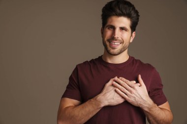 Gri arka planda izole edilmiş göğsünde el ele tutuşurken gülümseyen mutlu maskülen adam.