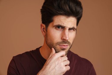 Düşünceli yakışıklı adam poz veriyor ve bej arka planda izole edilmiş kameraya bakıyor.