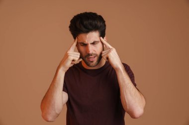 Başı ağrıyan, bej arka planda kalan şakaklarını ovuşturan memnun olmayan genç adam.