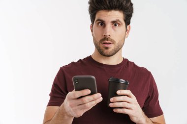 Beyaz arka planda izole edilmiş cep telefonu kullanırken kahve içen yakışıklı bir adam.