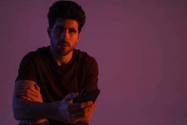 Mor arka planda izole edilmiş cep telefonu kullanırken poz veren erkeksi yakışıklı adam.