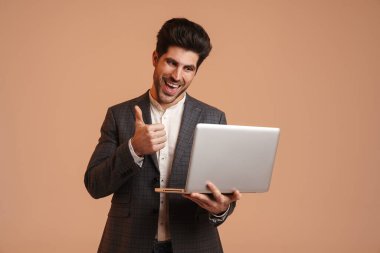 Bej arka planda izole edilmiş dizüstü bilgisayarla çalışan neşeli bir genç.