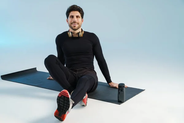 Jeune Sportif Souriant Avec Écouteurs Assis Sur Tapis Pendant Entraînement — Photo