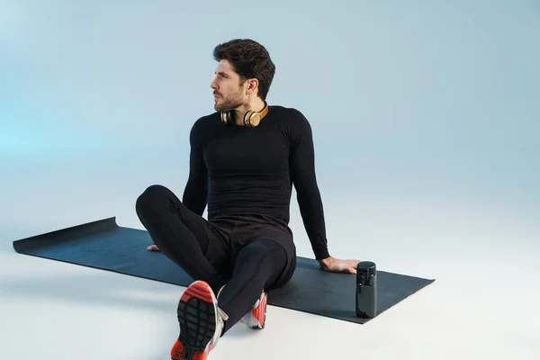 Jeune Sportif Avec Écouteurs Assis Sur Tapis Pendant Entraînement Isolé — Photo