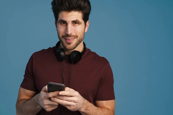 Pleased Handsome Man Headphones Using Mobile Phone Isolated Blue Background — Stock Photo, Image
