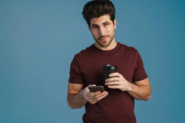 Pleased Handsome Man Drinking Coffee Using Mobile Phone Isolated Blue — Stock Photo, Image