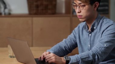 Ofiste otururken bilgisayarını karıştıran konsantre Çinli bir adamın yan görüntüsü.