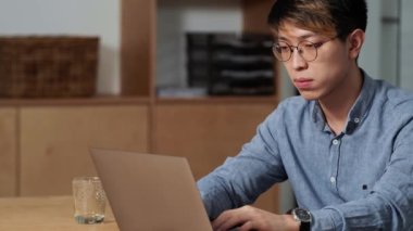 Ofiste otururken bilgisayarına bir şey yazan konsantre Çinli bir adamın yan görüntüsü.