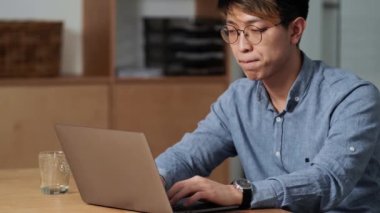 Ofiste otururken laptopta bir şeyler yazan kendinden emin Çinli bir adamın yan görüntüsü.