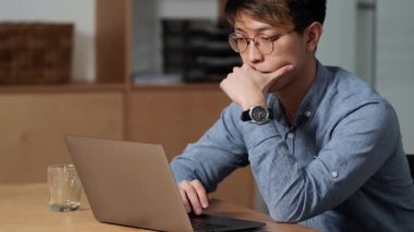 Konsantre olmuş Çinli bir adamın laptopta bir şeyler araklarken ve ofiste otururken başını dik tutarken yan görünüşü.