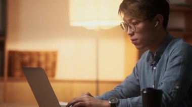 Kendine güvenen Asyalı bir adamın gece ofisinde otururken dizüstü bilgisayarını karıştırması.