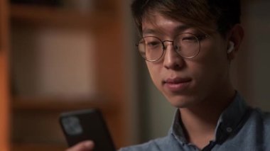 Gece ofisinde otururken telefona bakan konsantre Asyalı bir adamın yakın plan görüntüsü.