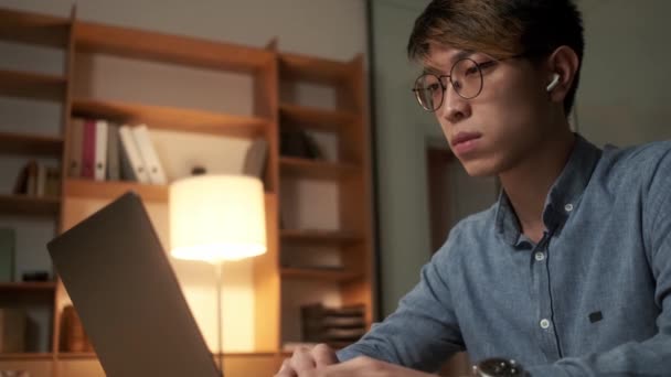 一个自信的中国男人坐在办公室里 一边翻看一边在笔记本电脑上翻找什么东西的侧面景象 — 图库视频影像