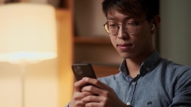 一个亚洲男人坐在夜间工作时在电话里打字的特写镜头 — 图库视频影像