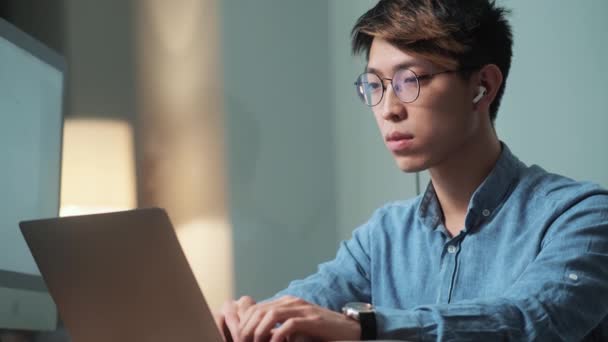 这位全神贯注的亚洲人坐在明亮的办公室里 一边翻阅着笔记本电脑里的什么东西 一边看着它 — 图库视频影像