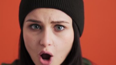 Şok olmuş bir kadının yakın çekim görüntüsü stüdyodaki kırmızı duvarın üzerinde tek başına duran kameraya bakıyor.