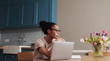 Güzel bir Afrikalı Amerikalı kadın dizüstü bilgisayarını evde mutfakta oturuyor.