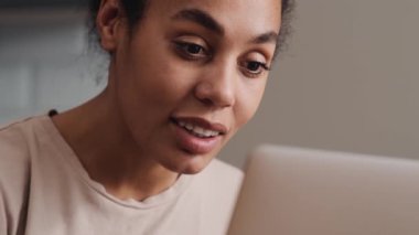 Pozitif bir Afrikalı Amerikalı kadının yakın plan görüntüsü laptopunu evde otururken kullanıyor.