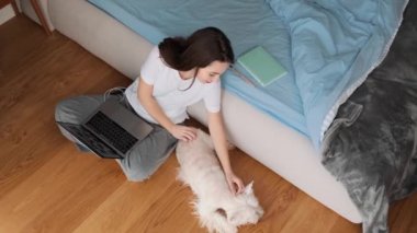 Çekici bir kadının en iyi görüntüsü, dizüstü bilgisayarını kulaklık takıp köpeğini evdeki yatak odasında okşarken kullanması.