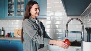 Mutfakta lavabonun yanında elma yıkayan gülümseyen kadın.