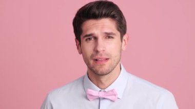 Papyon takmış kafası karışmış genç bir adam kameraya bakıyor. Stüdyoda pembe bir duvarın üzerinde tek başına duruyor.